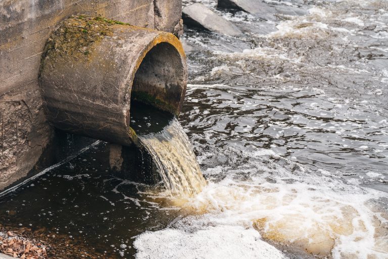 Dirty water flows from the pipe into the river, environmental pollution. Sewerage, treatment facilities.