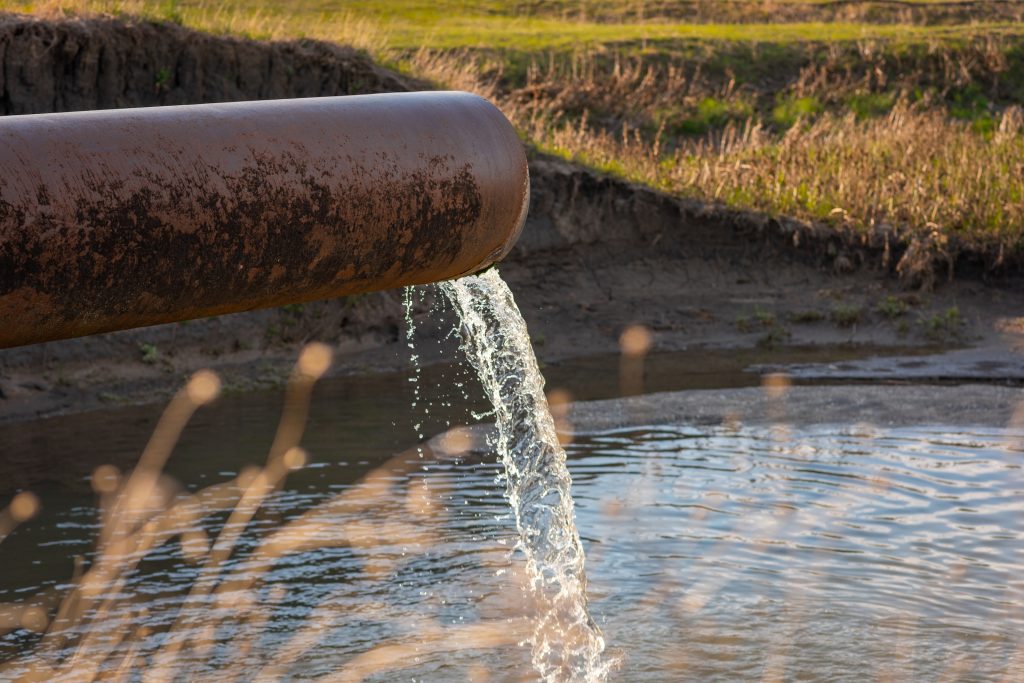 Toxicity Identification Evaluation Lab looking at water flows from a pipe into a river against the backdrop of nature. The concept of nature pollution, the release of waste into the water.